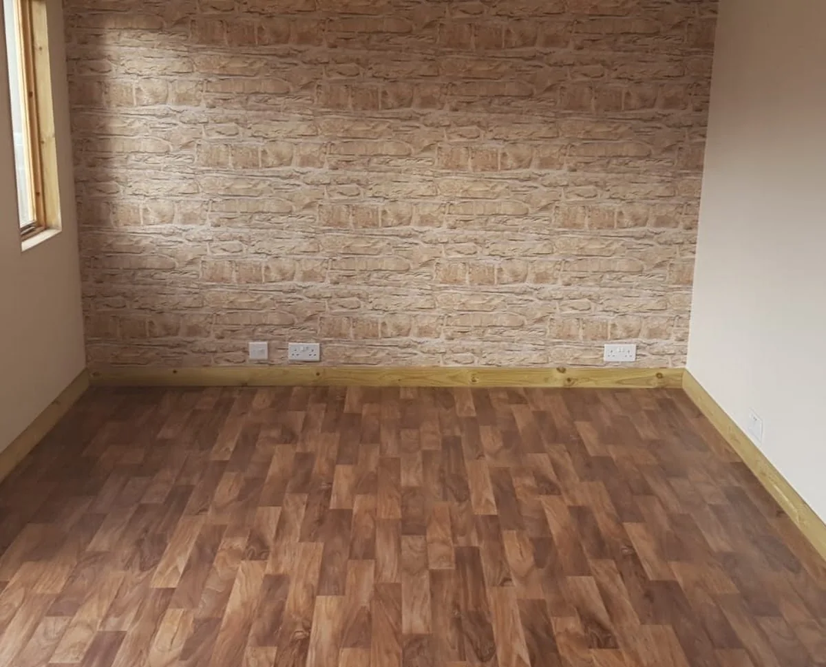 Finished room with a newly plastered ceiling, brick-effect feature wall and wood-effect flooring