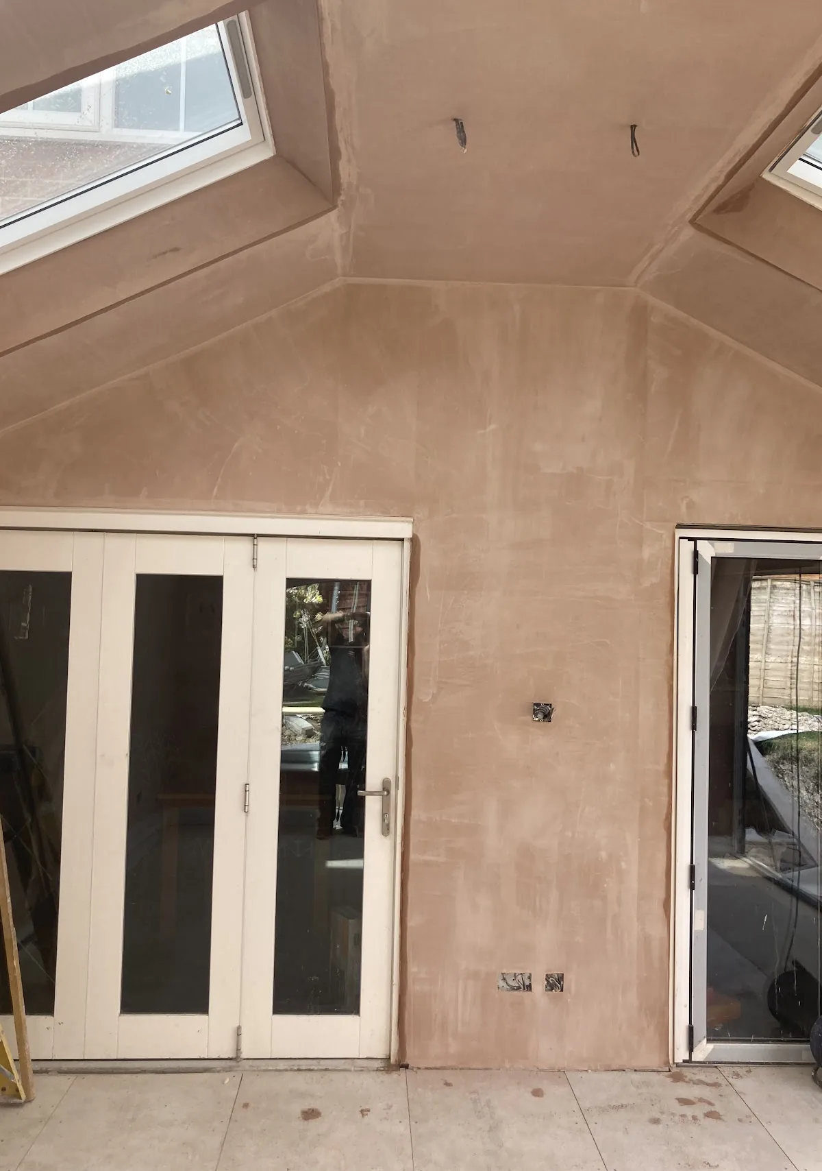 Sloped ceiling and wall freshly plastered beside a set of French doors