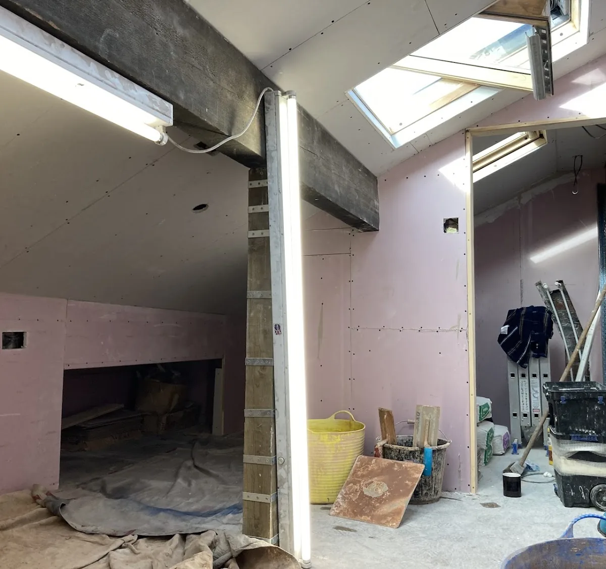 Loft room stripped back and prepared for plastering, with the chimney breast and Velux windows exposed
